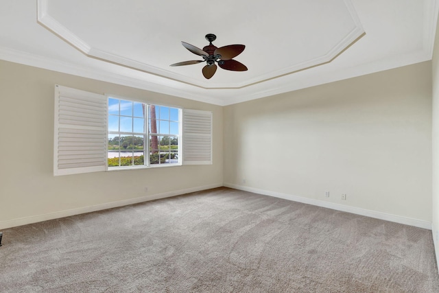 spare room with crown molding, baseboards, ceiling fan, a raised ceiling, and carpet