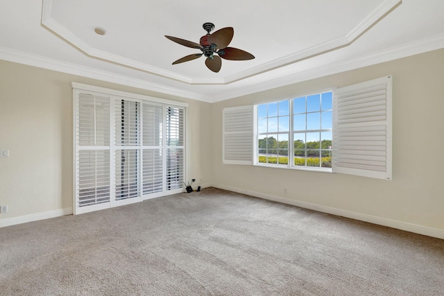 carpeted spare room featuring a ceiling fan, a tray ceiling, ornamental molding, and baseboards