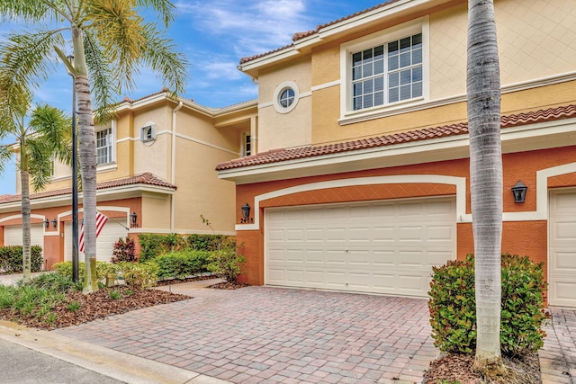 view of front of home with decorative driveway, a garage, stucco siding, and a tiled roof