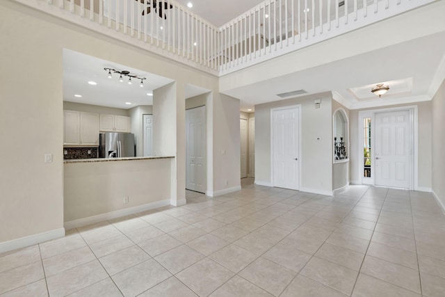 unfurnished living room with light tile patterned floors, baseboards, ornamental molding, and a towering ceiling