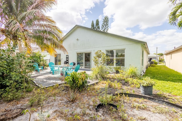 back of property featuring a lawn, a patio, and stucco siding