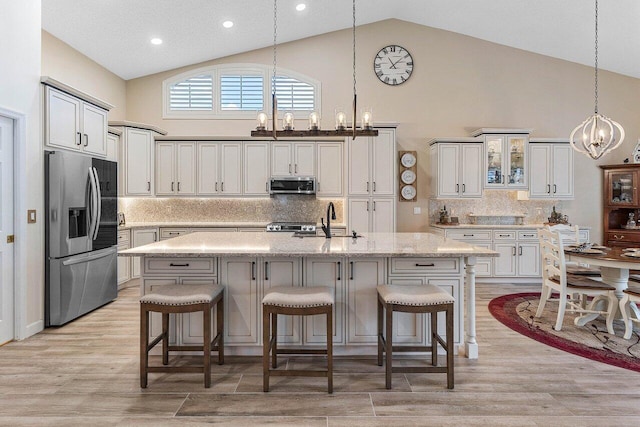 kitchen with appliances with stainless steel finishes, an inviting chandelier, a sink, light wood-style floors, and high vaulted ceiling