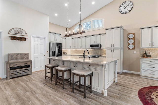 kitchen with a notable chandelier, appliances with stainless steel finishes, a sink, high vaulted ceiling, and tasteful backsplash