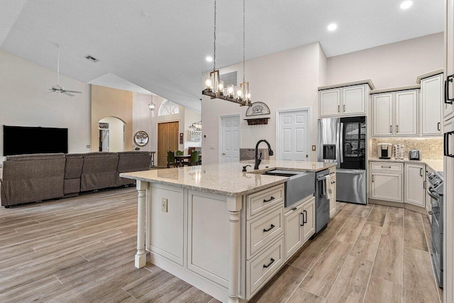 kitchen featuring a kitchen island with sink, high vaulted ceiling, light stone counters, a sink, and stainless steel appliances