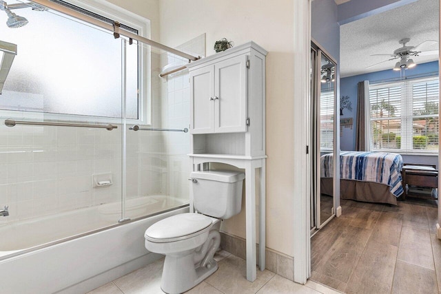 bathroom with connected bathroom, shower / bath combination with glass door, ceiling fan, toilet, and a textured ceiling