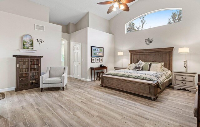 bedroom featuring light wood-style floors, arched walkways, high vaulted ceiling, baseboards, and visible vents
