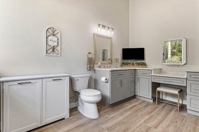 bathroom with a towering ceiling, toilet, wood finished floors, and vanity