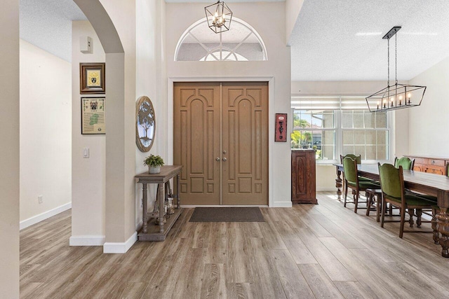 entryway featuring an inviting chandelier, arched walkways, a textured ceiling, baseboards, and wood finished floors