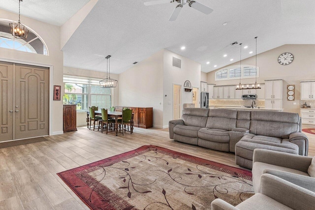 living area with visible vents, high vaulted ceiling, baseboards, ceiling fan with notable chandelier, and light wood-style floors