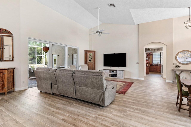 living area with a healthy amount of sunlight, a ceiling fan, visible vents, arched walkways, and high vaulted ceiling