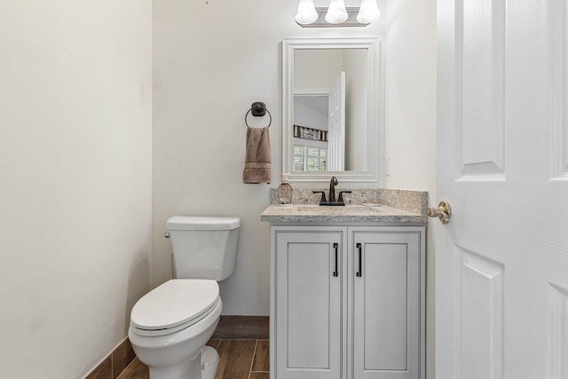 half bath with vanity, toilet, wood finished floors, and a chandelier