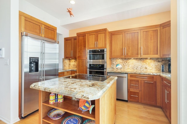 kitchen with stainless steel appliances, open shelves, brown cabinetry, a center island, and light stone counters
