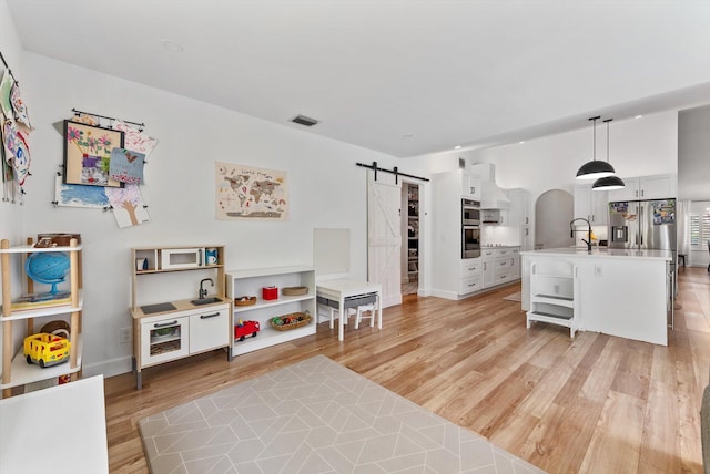 rec room featuring visible vents, a barn door, arched walkways, a sink, and light wood-style flooring