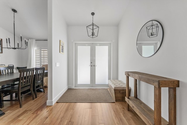 entrance foyer with an inviting chandelier, light wood-style flooring, baseboards, and french doors