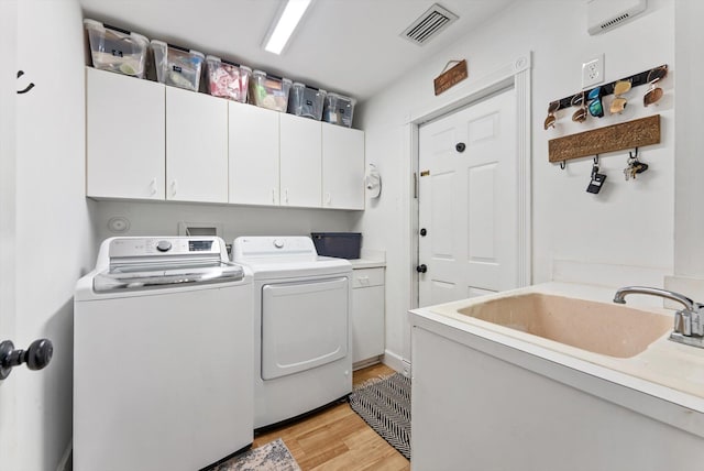 washroom with light wood-style floors, visible vents, cabinet space, and washer and clothes dryer