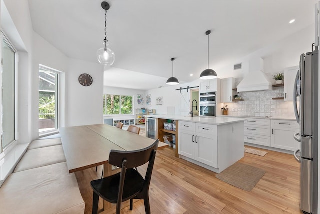 kitchen with open shelves, appliances with stainless steel finishes, a barn door, decorative backsplash, and custom exhaust hood