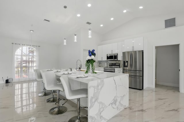 2449 SE Rock Springs Dr, Port Saint Lucie, FL 34952 - kitchen with stainless steel appliances, white cabinets, a breakfast bar area, pendant lighting, and an island with sink