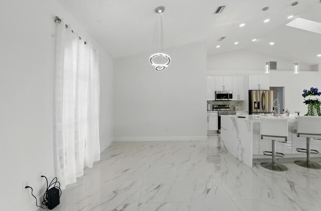 2449 SE Rock Springs Dr, Port Saint Lucie, FL 34952 - kitchen with stainless steel appliances, white cabinets, a breakfast bar, hanging light fixtures, and vaulted ceiling