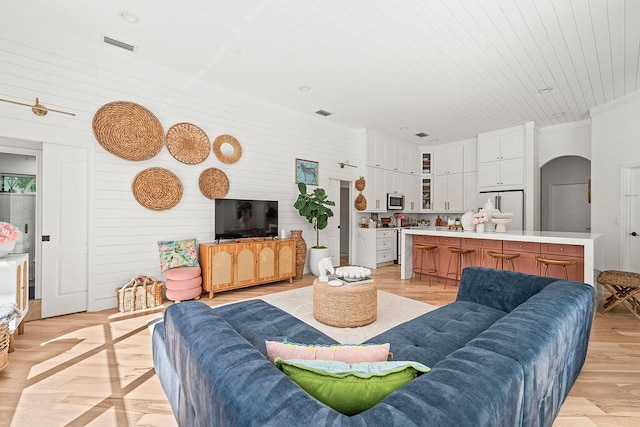 living room with arched walkways, visible vents, and light wood-type flooring