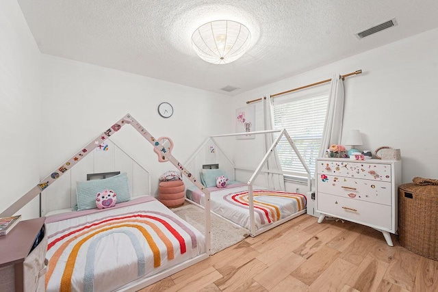 bedroom featuring light wood-type flooring, a textured ceiling, and visible vents