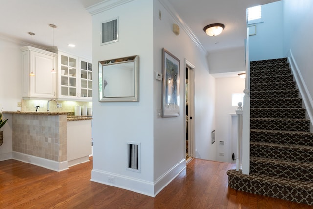 interior space with crown molding, baseboards, wood finished floors, and visible vents