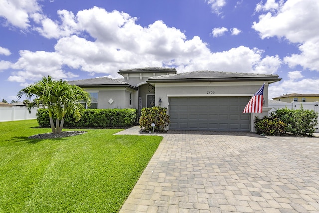prairie-style home with a garage, a front lawn, fence, decorative driveway, and stucco siding