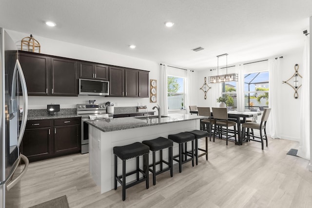 kitchen featuring a sink, appliances with stainless steel finishes, light wood-style floors, and dark stone counters
