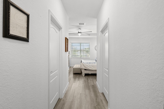 hall with visible vents, light wood-style flooring, a textured wall, and baseboards