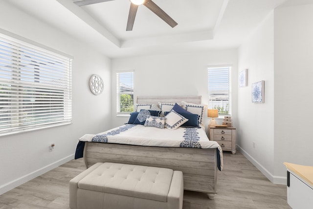 bedroom with a ceiling fan, baseboards, light wood-style flooring, and a raised ceiling