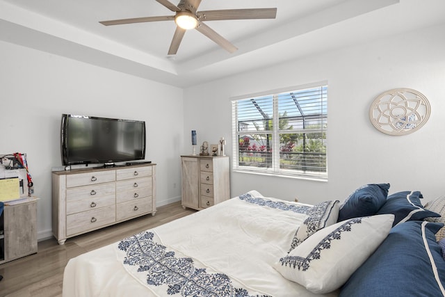 bedroom featuring baseboards, light wood-style flooring, ceiling fan, and a tray ceiling