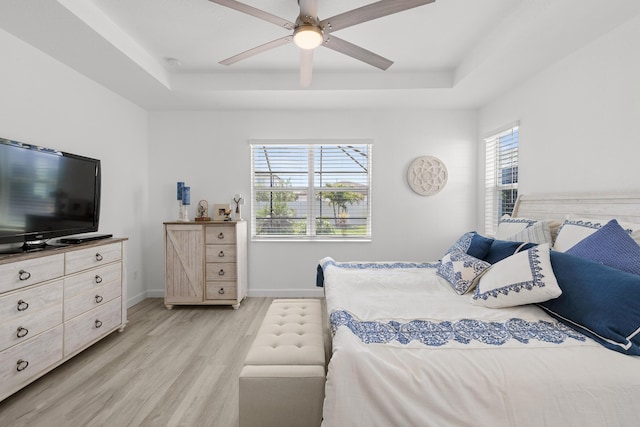 bedroom featuring ceiling fan, a raised ceiling, baseboards, and light wood-style flooring