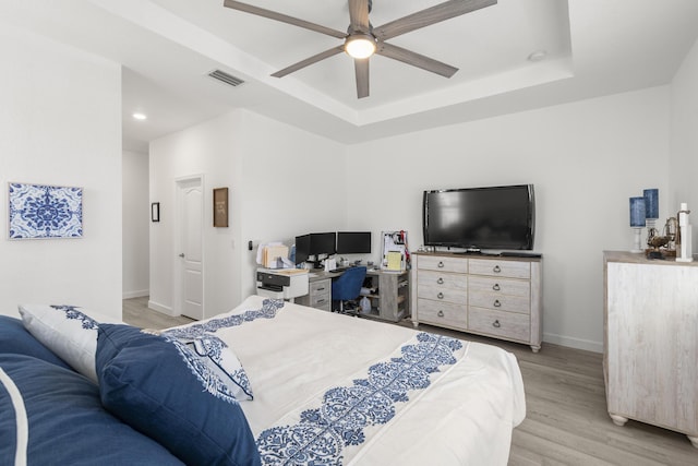 bedroom featuring visible vents, light wood-style floors, baseboards, ceiling fan, and a tray ceiling