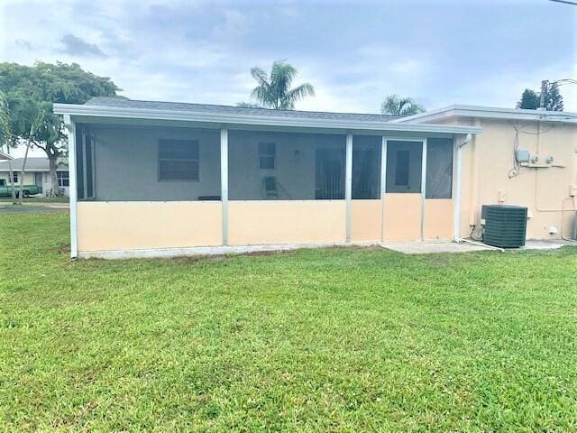 2821 Duke Ln, Delray Beach, FL 33445 - rear view of house with a sunroom, central AC unit, stucco siding, and a yard