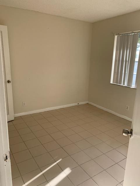 spare room with baseboards, a textured ceiling, and light tile patterned flooring