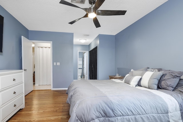 bedroom featuring a textured ceiling, visible vents, wood finished floors, baseboards, and ensuite bath