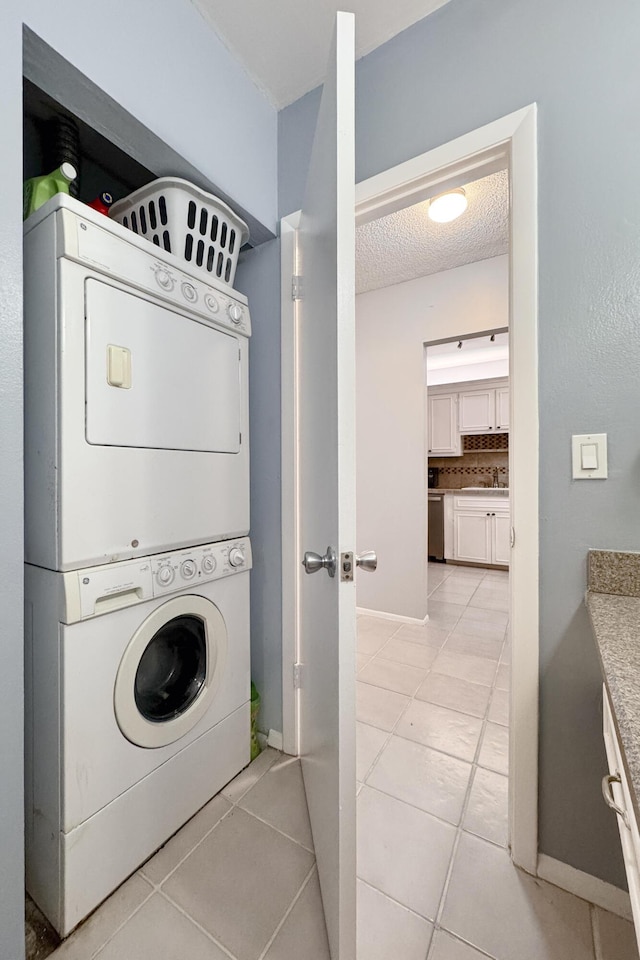 laundry room featuring laundry area, stacked washer and dryer, a textured ceiling, light tile patterned floors, and baseboards