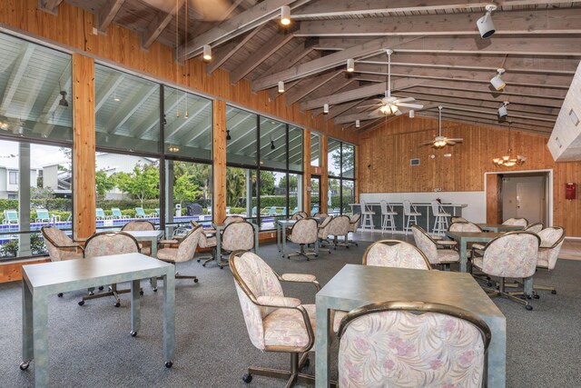 dining room featuring track lighting, high vaulted ceiling, wood walls, carpet, and a ceiling fan