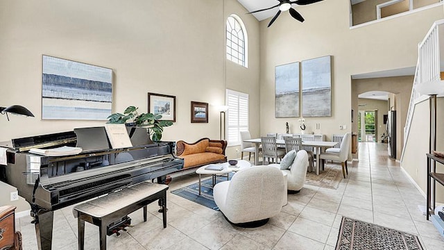 living area with a ceiling fan, arched walkways, a towering ceiling, plenty of natural light, and baseboards