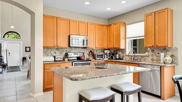 kitchen with stainless steel appliances, a sink, light tile patterned flooring, a breakfast bar area, and a kitchen island
