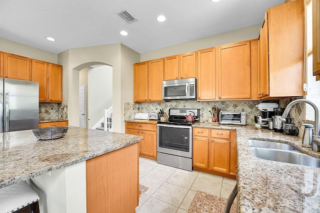 kitchen featuring appliances with stainless steel finishes, a sink, arched walkways, light stone countertops, and tasteful backsplash