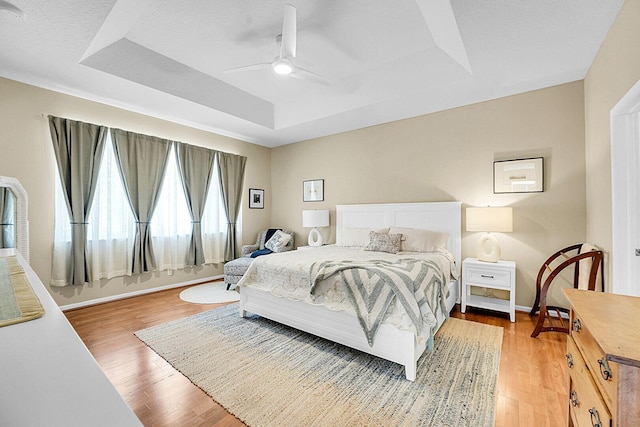 bedroom with a raised ceiling, wood finished floors, baseboards, and a ceiling fan