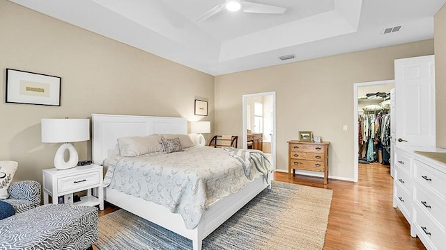 bedroom featuring a raised ceiling, light wood finished floors, a spacious closet, a closet, and a ceiling fan