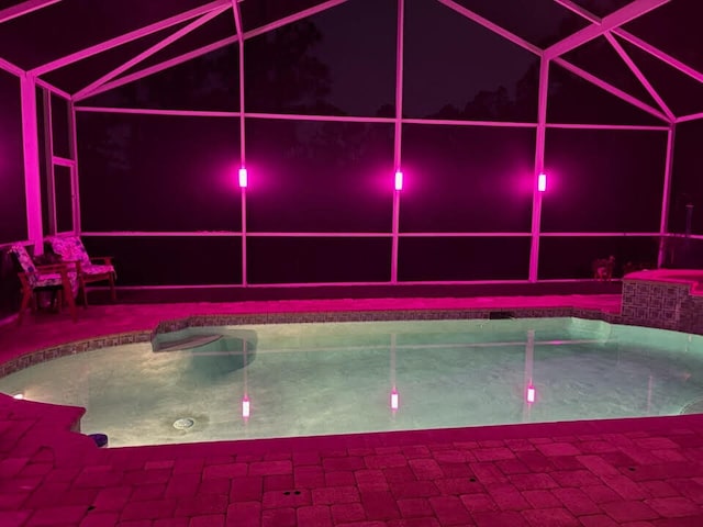 pool at night featuring a lanai, an outdoor pool, and a patio area