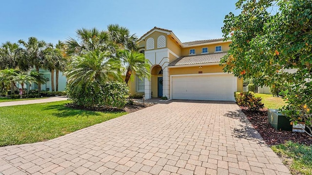 mediterranean / spanish-style home with decorative driveway, a front lawn, stucco siding, and a tile roof