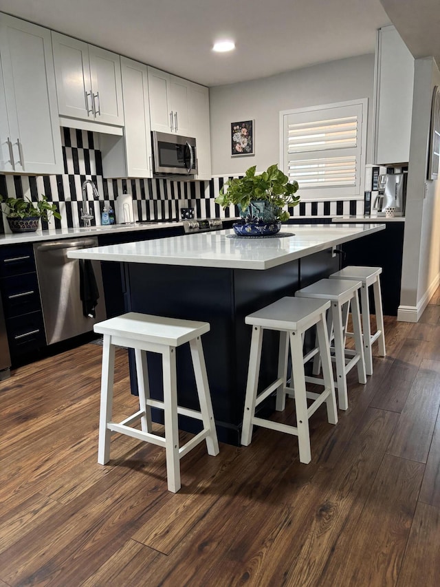 kitchen featuring decorative backsplash, a kitchen island, dark wood finished floors, light countertops, and stainless steel appliances