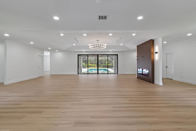 unfurnished living room featuring light wood-style flooring, recessed lighting, a tray ceiling, baseboards, and a chandelier