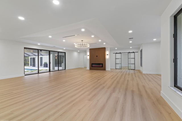 unfurnished living room featuring a barn door, recessed lighting, light wood-type flooring, baseboards, and a chandelier