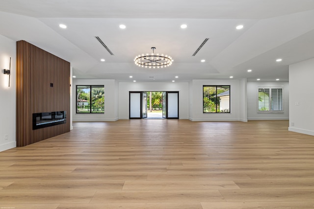 unfurnished living room featuring light wood-style floors, plenty of natural light, recessed lighting, a fireplace, and a chandelier