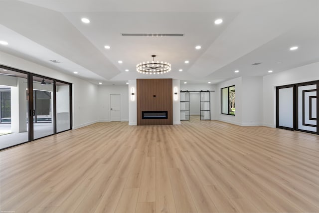 unfurnished living room with a barn door, light wood finished floors, recessed lighting, baseboards, and a chandelier