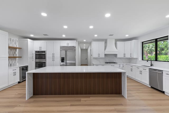 kitchen with stainless steel appliances, beverage cooler, premium range hood, a kitchen island, and white cabinetry